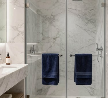 A luxury modern bathroom renovation in a Southern European / Spanish home, featuring marble walls, a walk-in rain shower, and elegant dark navy blue towels, clean and bright natural lighting.