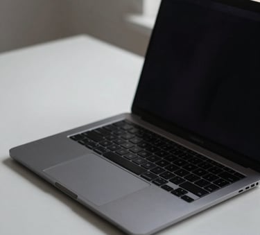 A close-up photograph of a clean, minimalist workspace. A deep charcoal laptop sits on a pale mist colored desk. Soft natural light illuminates the scene, creating a professional and focused atmosphere.