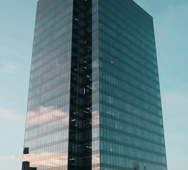 A high-end architectural view of a modern glass skyscraper in Vilnius, reflecting the sky, representing the established presence of the Bank of Lithuania and financial stability. Sophisticated lighting, incorporating deep teal and black tones in the shadows and cyan highlights on the glass.