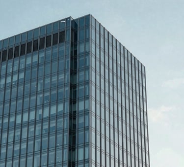 A minimalist architectural detail photograph showing the corner of a modern glass skyscraper against a clear sky in a North American city. The focus is on the precision of the steel construction, using a palette of steel blue and light grey to convey stability and excellence.
