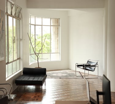 Modern minimalist living room featuring mid-century furniture and a leather daybed by large windows.