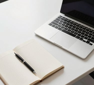 A top-down professional photography shot of a clean, modern white desk with a laptop, a notebook, and a sleek pen. Bright natural light floods the North American office space, creating a professional and clear atmosphere with soft shadows.