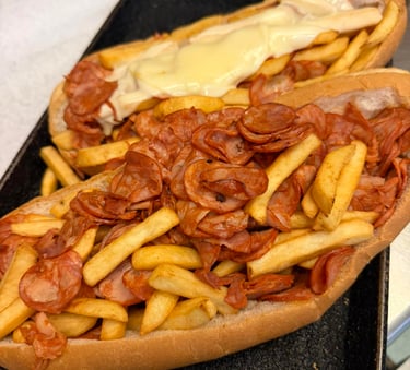 Two loaded submarine sandwiches topped with crispy french fries, sliced pepperoni, and melted cheese sauce.