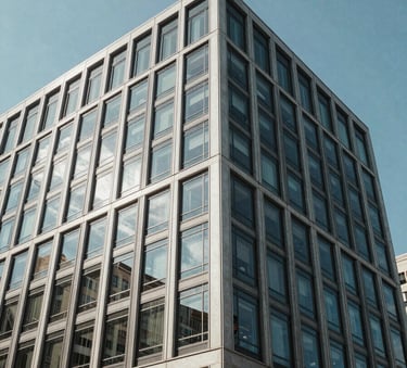 A minimalist, low-angle photograph of a modern commercial office building in a North American city, featuring clean glass windows and steel structures under a clear blue sky.