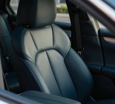 A close-up, high-angle shot of a luxury car interior. The leather seats are perfectly conditioned with a soft matte finish. Soft daylight highlights the intricate stitching and the pristine condition of the dashboard. The colors feature deep blacks and #003D5B blue accents in the cabin lighting. The vibe is immaculate and premium.