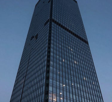 A high-angle architectural shot of a modern glass skyscraper reflecting a deep navy and slate blue sky at twilight, emphasizing professional exclusivity and scale.