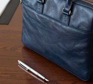 A high-quality close-up photograph of a professional leather briefcase and a silver fountain pen resting on a polished mahogany desk. The setting is a sophisticated North American corporate office in Kirkland, Washington. The lighting is soft and natural, emphasizing textures of leather and wood. Colors include deep navy and muted blue accents.