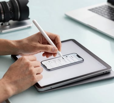 A professional photograph of a designer's hands using a stylus on a high-resolution tablet to sketch a sleek mobile app interface. The setting is a bright, modern studio in North America with light blue and silver tones in the environment.