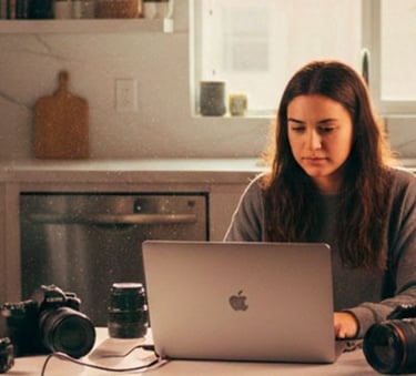 Professional photographer editing photos on a laptop with cameras and softbox lighting in a kitchen studio.