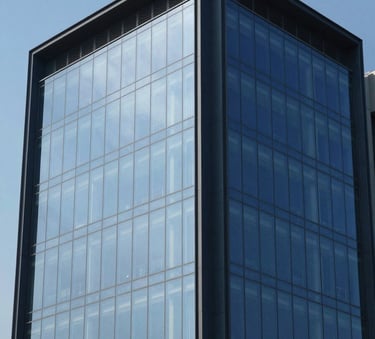 A crisp architectural photograph of a modern corporate headquarters in Pakistan. The building features large glass panels reflecting a clear blue sky, with structural accents in dark navy blue. Clean, minimalist composition.