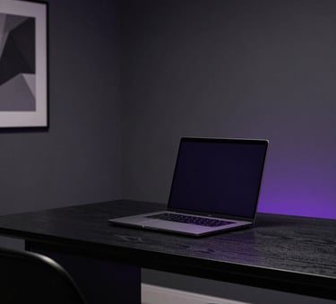 A sophisticated minimalist home office with dark grey walls and a high-end laptop on a black wooden desk, illuminated by subtle purple ambient lighting. North American / International setting.