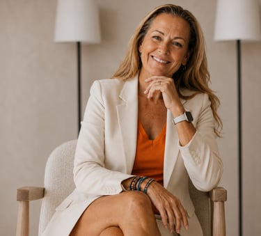 Professional portrait of a smiling woman seated in a modern neutraltoned chair, wearing a cream suit