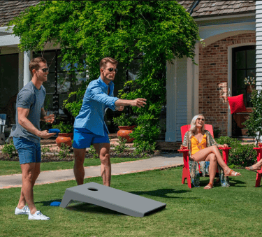 Žmonės žaidžia cornhole žaidimą kieme. Meta žaidimo maišelį į lentą