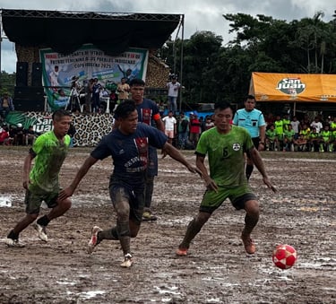 Muddy soccer players competing for the ball during an indigenous community tournament match.