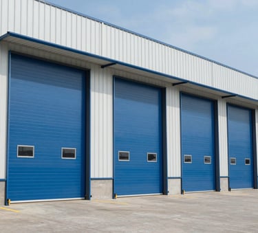 A wide-angle professional photograph of a commercial warehouse in the North American / US region, featuring large industrial slate blue rolling steel doors. The lighting is bright daylight, highlighting the clean, modern architecture.