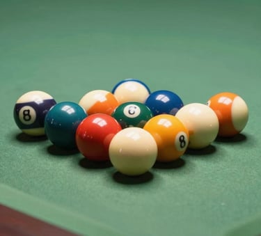 A macro photograph of professional billiard balls tightly racked on a table with sage green felt. The lighting is warm and focused, highlighting the sophisticated bronze-toned wood of the table frame.