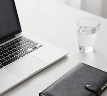 A crisp, professional high-angle shot of an organized desk with a high-end laptop, a leather-bound notebook, and a glass of water. Minimalist and corporate style with a palette of #F8F8F8 and #1A202C.