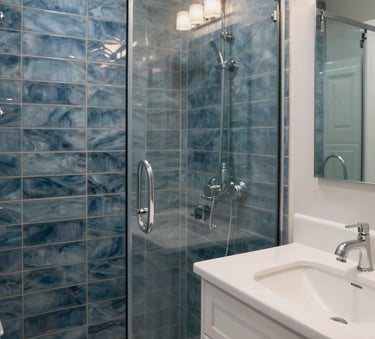 A high-end bathroom renovation in a North American / Canadian (with South Asian cultural influence) home. The scene features steel blue tiles, a modern glass shower, and crisp off-white vanity. Bright, professional lighting highlights the craftsmanship.
