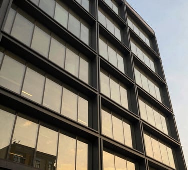 A low-angle shot of a sleek, modern South African commercial building facade with dark grey steel beams and gold-tinted architectural glass, reflecting a clear sky. Luxury minimalist style.