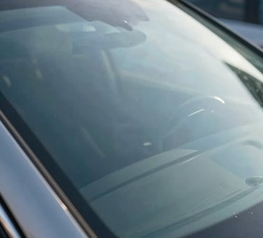 A crisp, detailed close-up of a flawless luxury car windshield reflecting a clear blue sky and modern North American architecture, symbolizing clarity and precision in glass replacement.