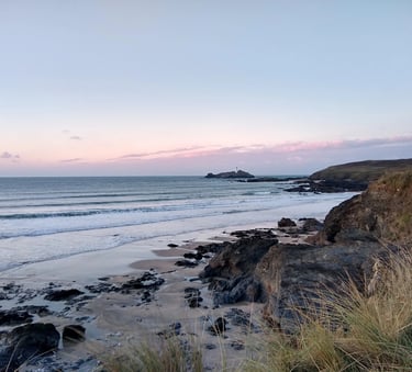 Scenic coastal view of Godrevy Lighthouse at sunset from a rocky beach in Cornwall, England.