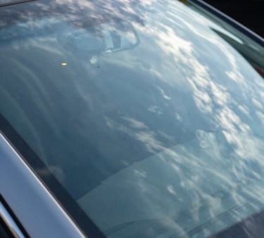 Close-up of a perfectly clean and shiny luxury car windshield reflecting a bright blue North American sky with light wispy clouds, emphasizing safety and clarity, high-end photography, sharp focus.