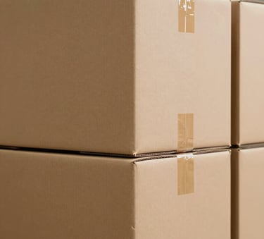 A close-up shot of heavy-duty, corrugated industrial shipping boxes stacked neatly in a clean warehouse. The lighting is bright and professional, highlighting the structural integrity and thick walls of the cardboard. The color palette includes #6B4D3C brown and #A08D7D beige, conveying a sense of reliability.