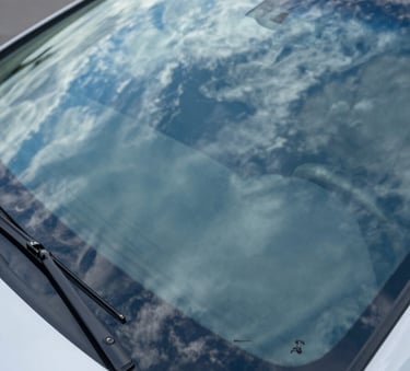 High-angle shot of a pristine, newly installed car windshield reflecting a clear bright blue sky and wispy white clouds, emphasizing crystal clarity and safety, North American setting.