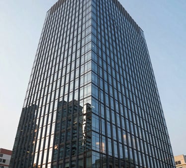 A wide-angle, high-definition photograph of a sleek, modern commercial glass building in Noida, South Asian / Indian urban architecture, bright sunlight reflecting off windows, professional photography.
