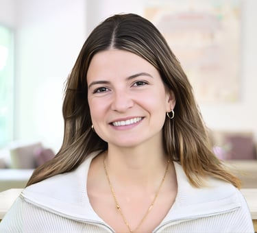 A smiling professional woman with brown hair wearing a white zip-up sweater and gold jewelry.