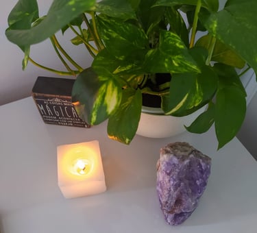 um cenario de uma vela, cristal ametista e uma planta em cima de uma mesa