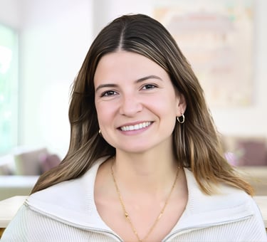 Smiling professional woman with brown hair and gold jewelry in a bright office.