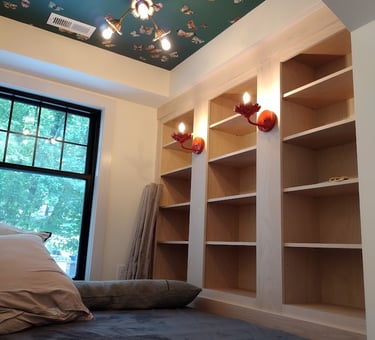 Cozy reading nook featuring built-in bookshelves, butterfly wallpaper ceiling, and red bird wall sconces.