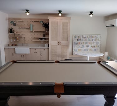 Modern game room with a grey billiard table, wet bar with pegboard shelving, and stylish cane cabinet.