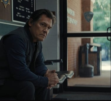 Josh Brolin sits pensively in a police station lobby, hands clasped, while two blurred figures talk