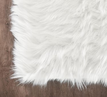 Soft white faux fur rug with shaggy texture placed on a dark brown hardwood floor.