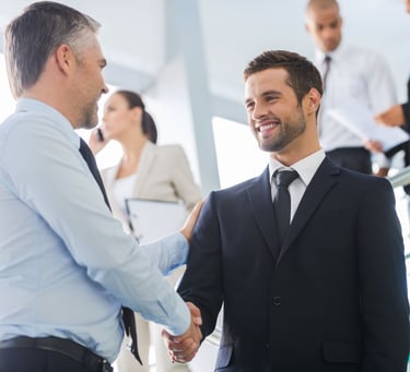 Two smiling businessmen in suits shaking hands in a professional office setting.