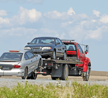 A Surrey tow truck carrying a car with a flat bed