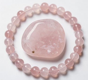 Pink rose quartz beaded bracelet surrounding a polished heart-shaped crystal stone on white background.