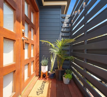 Private entrance at Marche Home Stay with a welcome mat, potted plants, and cosy outdoor lighting.