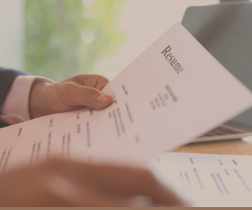 a person holding a resume in front of a laptop