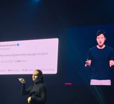 an ASL interpreter at a tech conference in front of a screen that shows a speaker next to a tweet