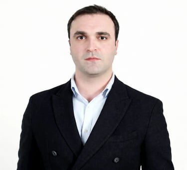 Professional headshot of a man in a black blazer and light blue shirt against a white background.