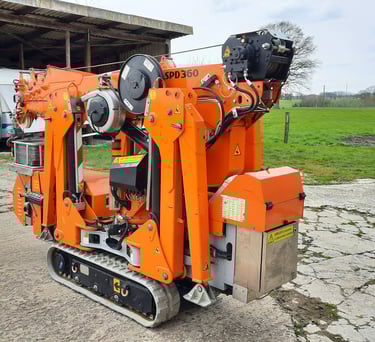 Kompakter oranger Minikran SPD360 auf Raupenketten, zusammengefaltet vor einer Scheune.