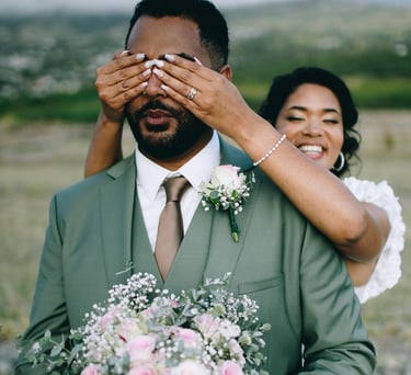 Mariée couvre les yeux du marié en costume vert sauge, first look champêtre.