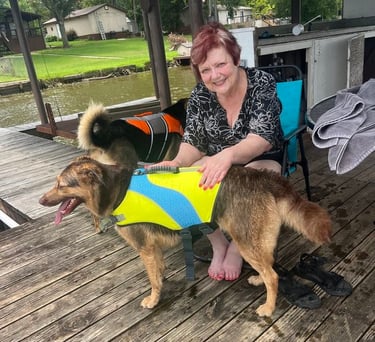 Photo of Debbie, seated on a lake dock, tending to two dogs wearing colorful life vests.