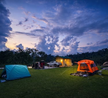 Camping site at dusk with multiple colorful tents, parked vehicles, and a small building under a dramatic, cloud-filled sky.