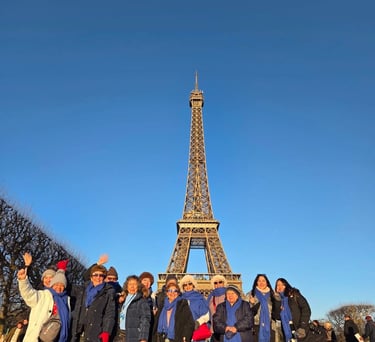 Un grupo de turistas con bufandas azules posan frente a la Torre Eiffel bajo un cielo azul despejado en París.