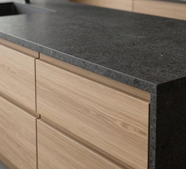 A close-up of a high-end kitchen island with a smooth charcoal stone countertop and minimalist light oak drawers, soft natural light, European interior design style.