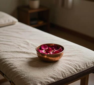 A serene treatment room featuring low lighting, a comfortable mat, and a small copper bowl with rose petals, South Asian / Tamil Nadu, India.